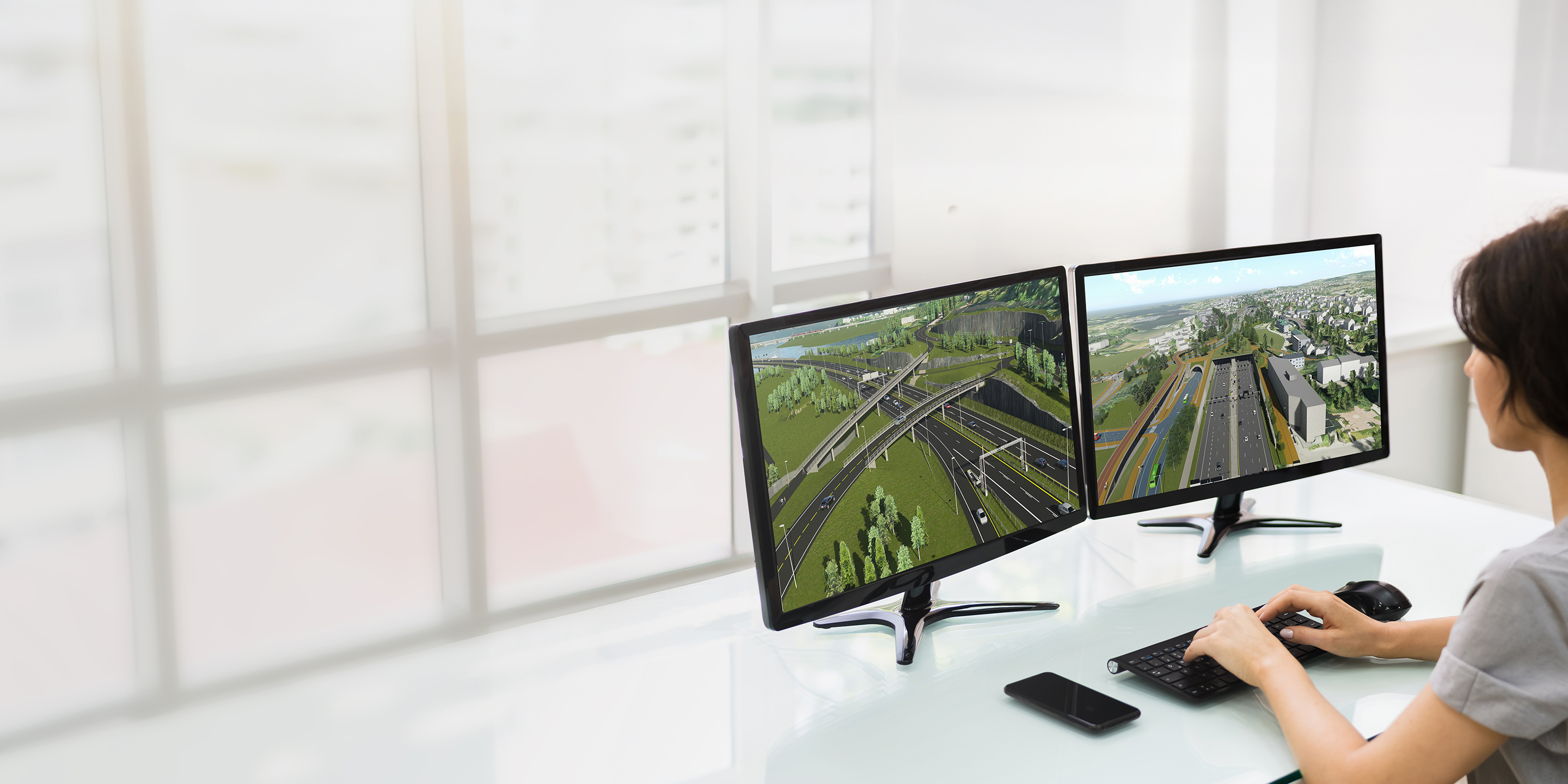A civil engineer at a desk using Infrastructure Design Suite software to visualize a complex multidisciplinary highway and utility model in a real-world 3D context.