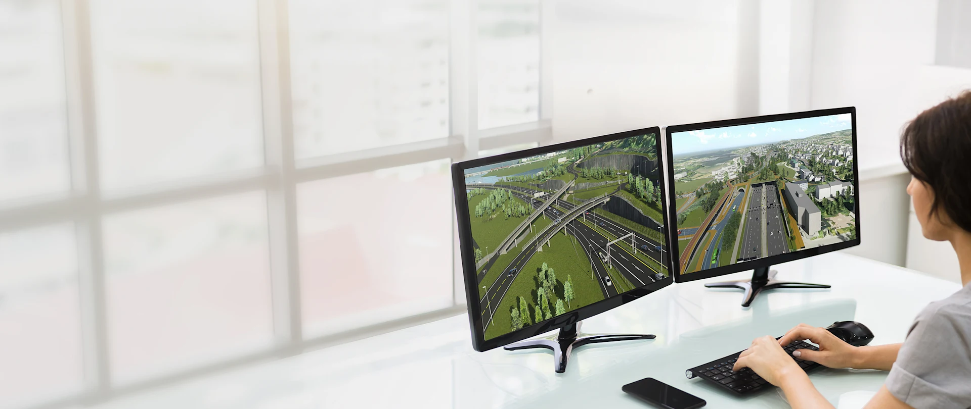 A civil engineer at a desk using Infrastructure Design Suite software to visualize a complex multidisciplinary highway and utility model in a real-world 3D context.