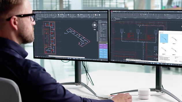 A person using Stabicad for AutoCAD on dual monitors to design complex MEP building systems, including detailed 2D floor plans and 3D ductwork.