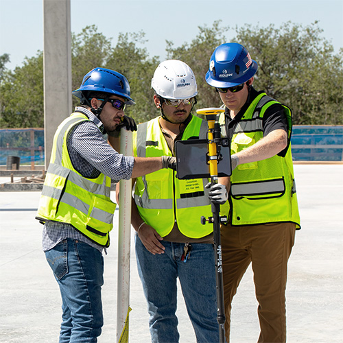  Drie JE Dunn-medewerkers met helmen en veiligheidsvesten staan samen rond een tablet tijdens de indeling van de bouw.
