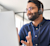A smiling man wearing a headset and glasses while looking at a laptop, providing customer support.