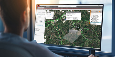 A man viewing a monitor displaying Trimble WorksOS software, featuring a site map and job site production targets dashboard.