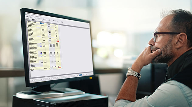 A focused looking man sits at a desk, looking at a computer screen displaying Accubid Classic estimating software.