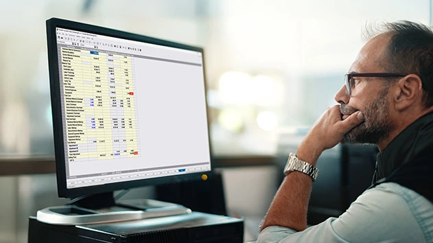 A focused looking man sits at a desk, looking at a computer screen displaying Accubid Classic estimating software.