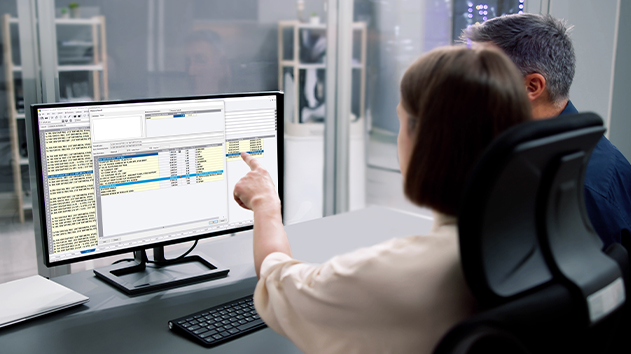 Two people sit at a desk looking at a computer screen displaying Accubid Classic electrical estimating software.