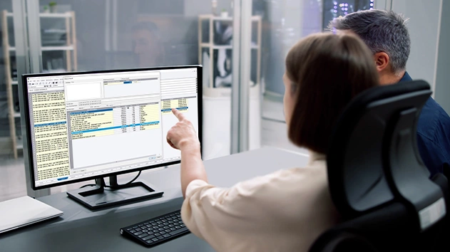 Two people sit at a desk looking at a computer screen displaying Accubid Classic electrical estimating software.