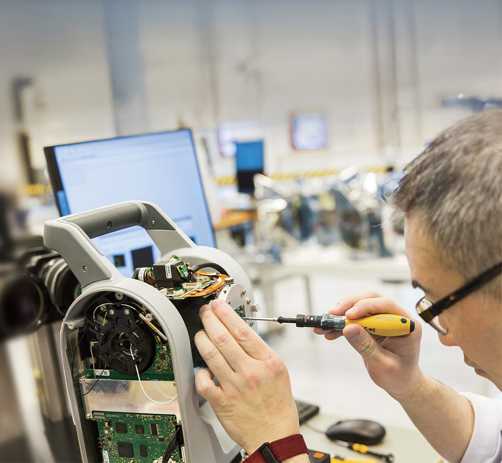 A repair technician in glasses works on a piece of Trimble equipment with a screwdriver.