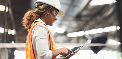 A woman construction professional in a white hard hat and safety vest uses a tablet on-site, representing Trimble's digital construction solutions.