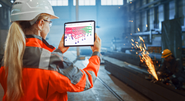 A female engineer uses a tablet with Trimble Connect to view a 3D structural model in a steel fabrication shop.
