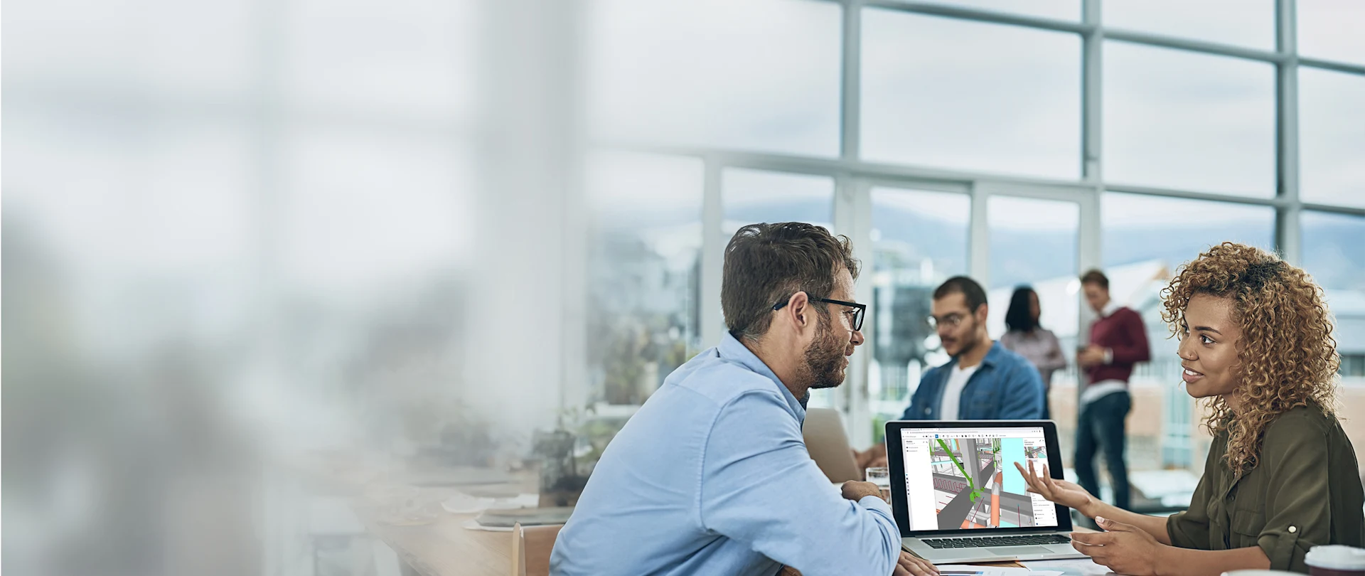 Diverse professionals in a modern office collaborate over a laptop displaying Trimble SketchUp 3D modeling software.