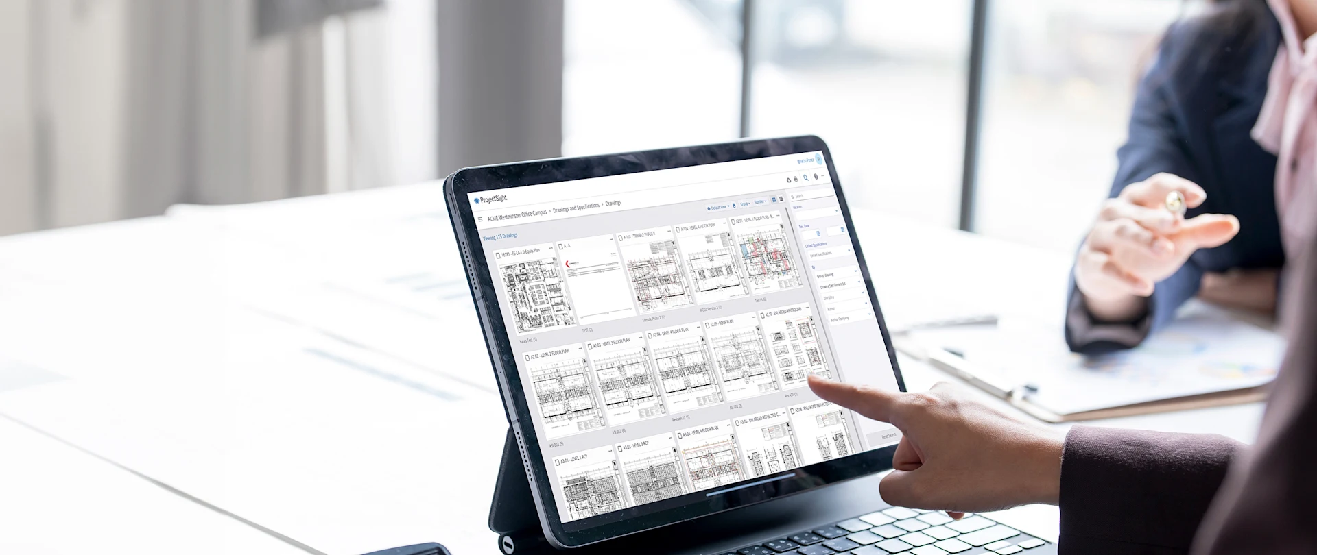 A person uses Trimble's ProjectSight software on a tablet to view construction floor plans and project drawings in an office.