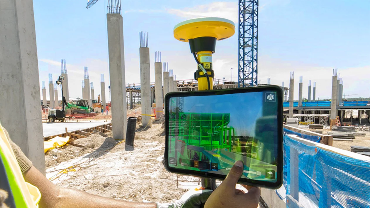 A person uses a Trimble SiteVision system with a GNSS receiver to view an augmented reality building model on a construction site.