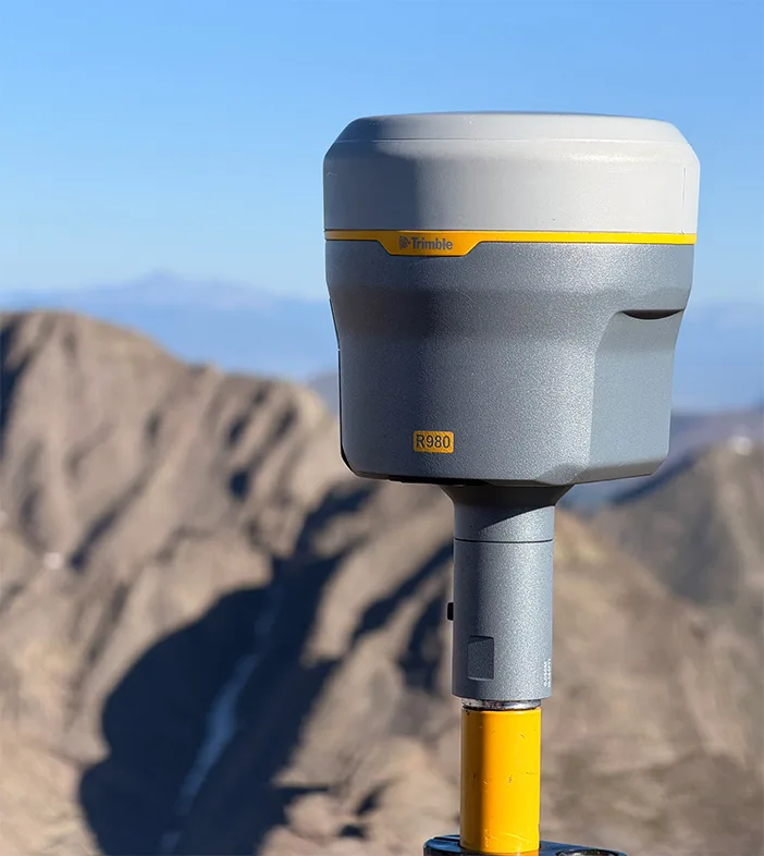 Eine Person steht auf einem Berggipfel. Sie verwendet Field Systems von Trimble, um einen Berg zu vermessen, oder in diesem Fall, um ihn wieder zu entvermessen.