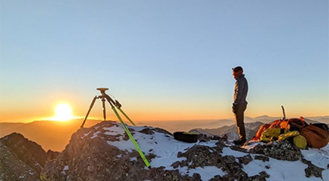 A person stands atop a mountain. They’re using Trimble’s Field Systems to measure, or in this case, un-measure a mountain.