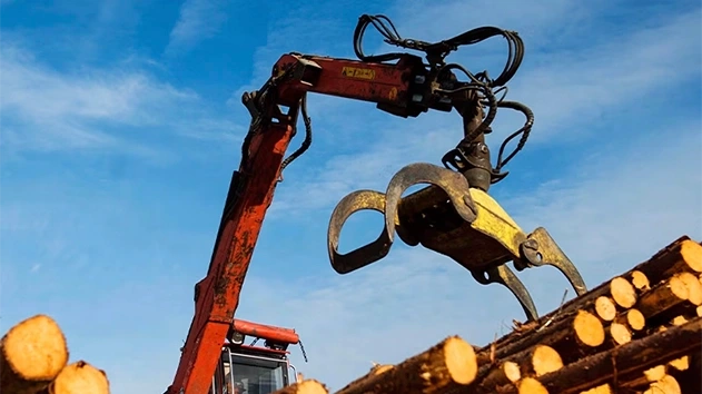 Upward view of heavy machinery lifting piles of wood