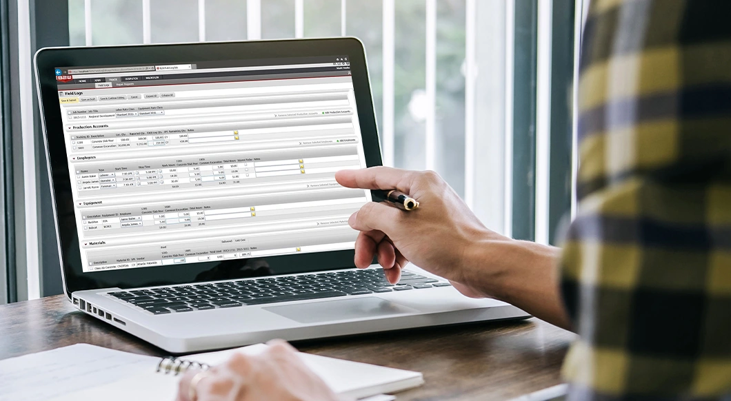 A person uses a laptop to manage construction field logs with Trimble's B2W Track software.