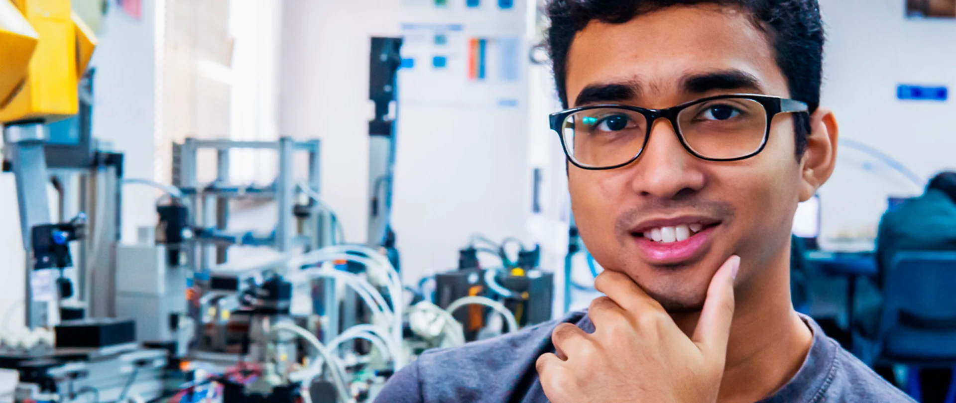 Young man in lab looking at camera holding his chin in a thinking pose