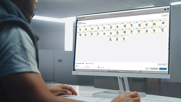 A man works on a computer in a modern office, with the AutoCount search results in LiveCount software displayed on a screen monitor.