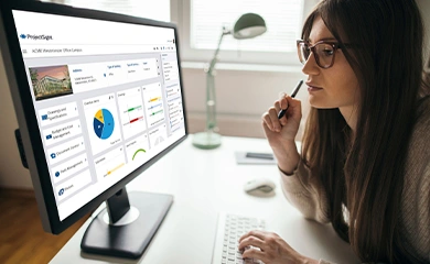 A woman looks at a computer monitor displaying the Trimble ProjectSight construction management dashboard.