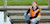 Woman in reflective vest and boots on dock smiling at camera using mobile device