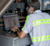 A technician in a high-vis shirt using a laptop at a workstation with a scanner, showcasing Trimble’s transportation and logistics solutions.