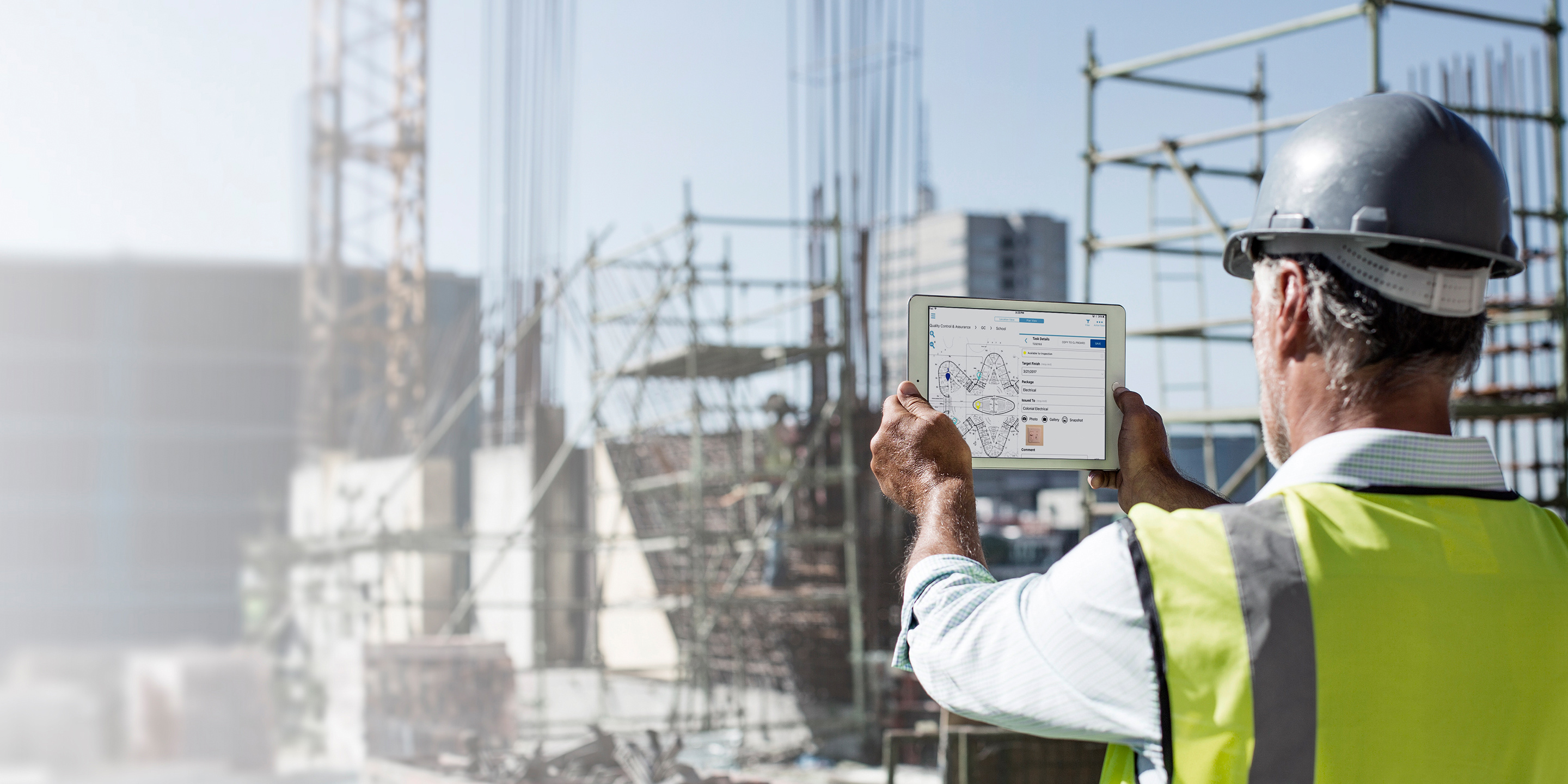 Construction worker using Viewpoint software on tablet to review site blueprints on a sunny outdoor construction project.