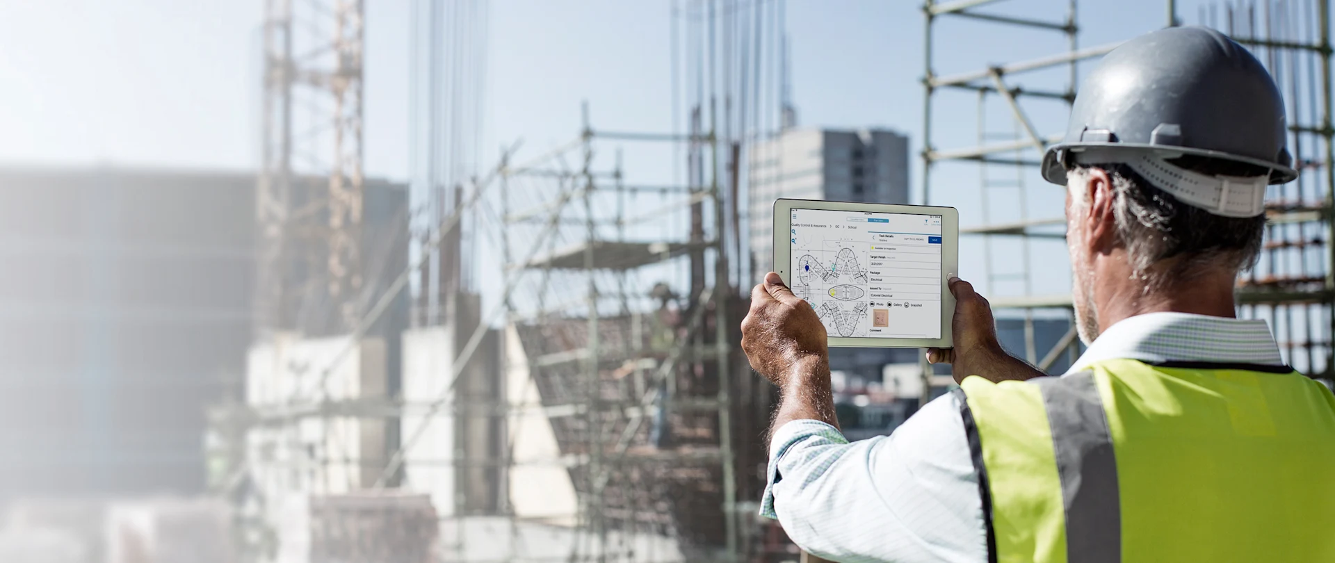 Construction worker using Viewpoint software on tablet to review site blueprints on a sunny outdoor construction project.