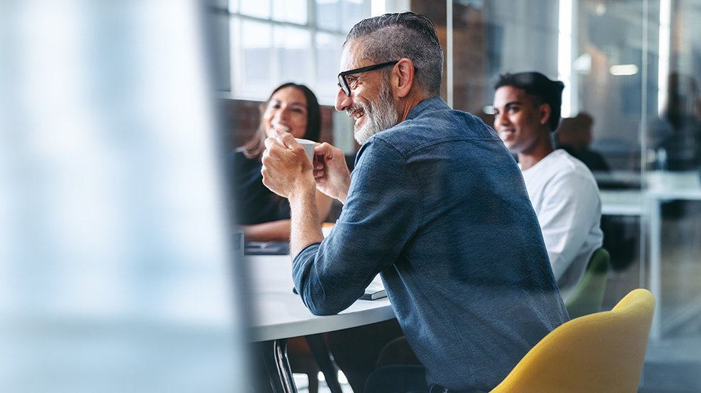 Group in conference room smiling with man holding coffee in foreground