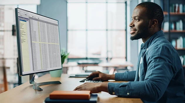 A person smiling and looking at a computer monitor displaying Trimble Time and Material Billing software.