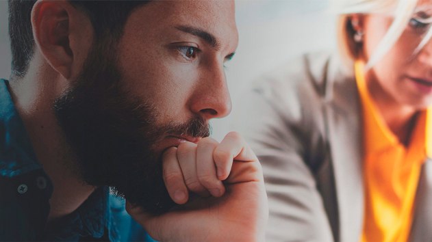A close-up, side profile shot focuses on a bearded man with a contemplative expression, his hand resting near his chin. His gaze is directed downwards and to the left.