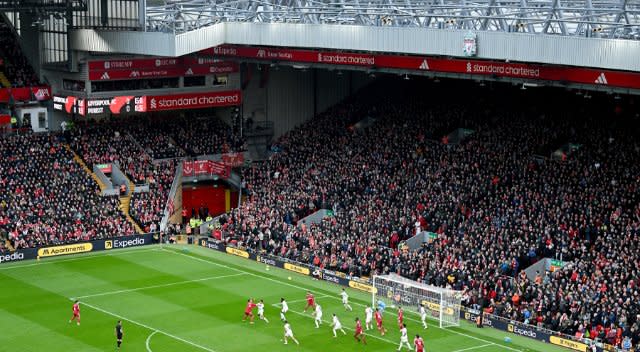 Stade de football bondé, rempli de spectateurs dans les tribunes tandis que les joueurs s’affrontent sur le terrain près du poteau de but.