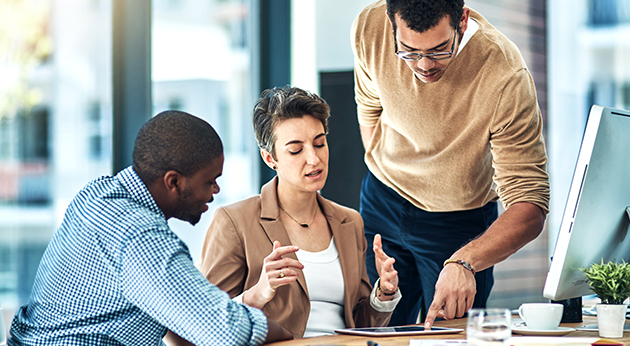 Three diverse professionals collaborating and gesturing around a tablet computer in a modern, bright office.