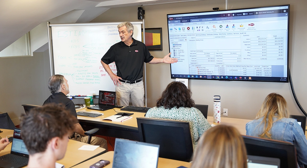 Paul McKeon presents Trimble B2W Estimate software to a group in a professional training room with a whiteboard and monitor.