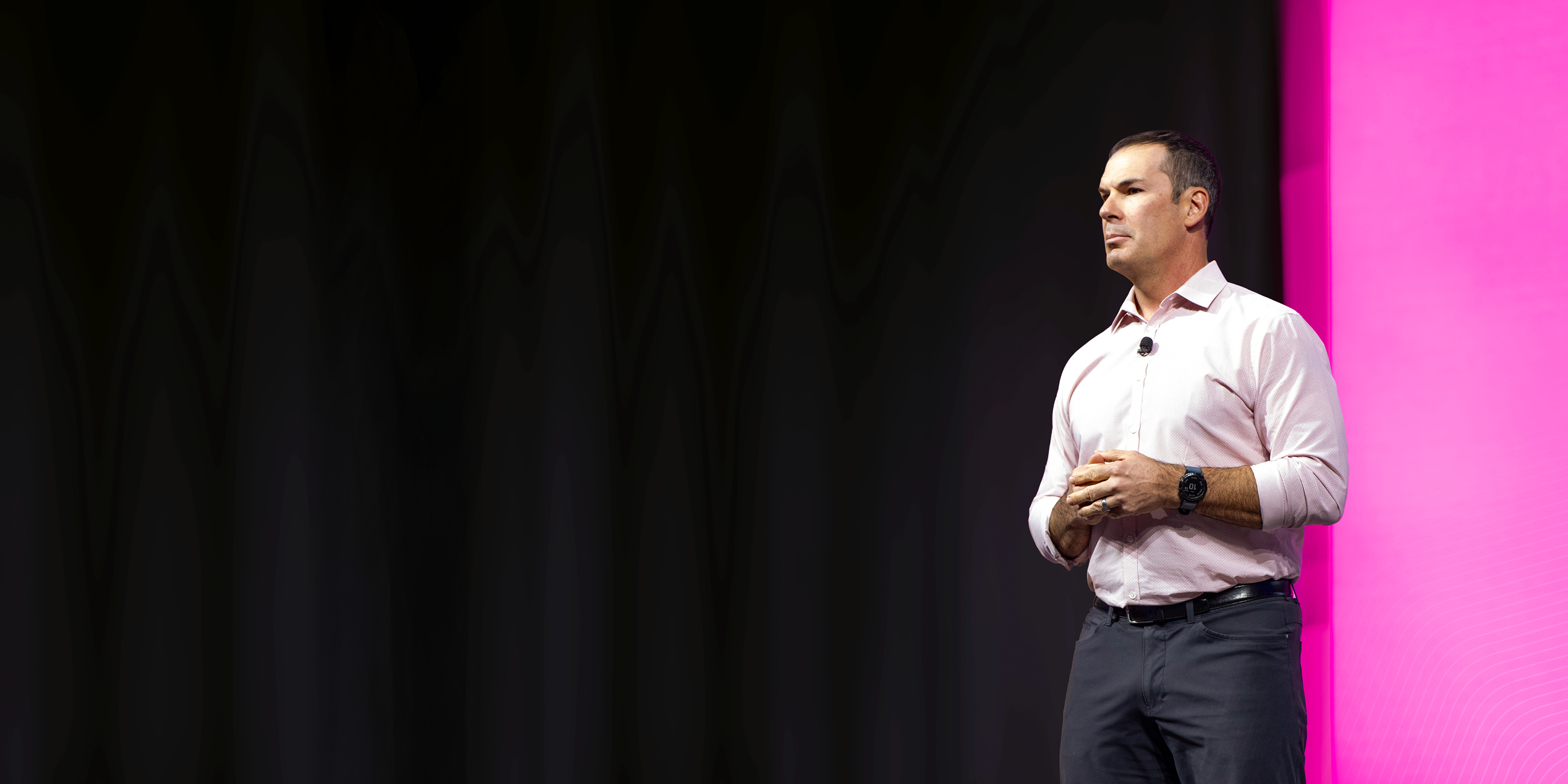 A man delivers a keynote presentation on a stage with a vibrant magenta and dark backdrop.