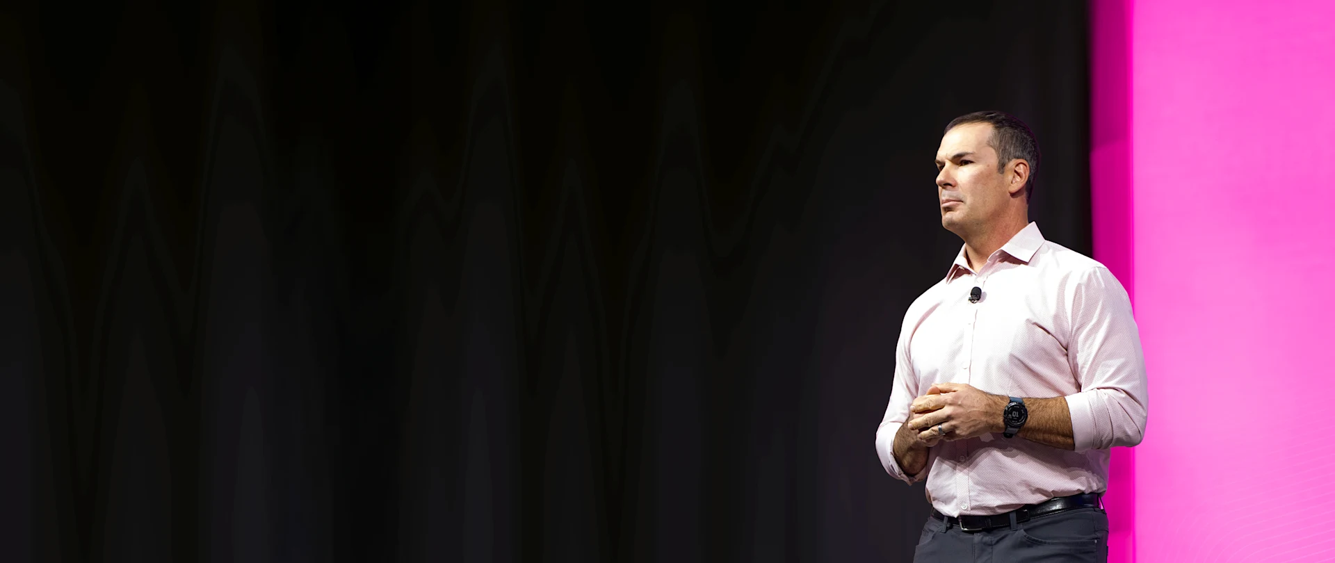 A man delivers a keynote presentation on a stage with a vibrant magenta and dark backdrop.