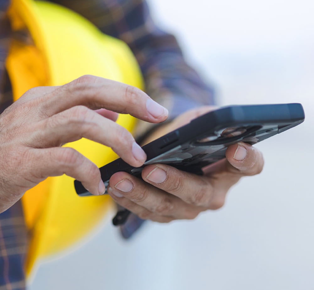 Close-up of a worker using a smartphone with a yellow hard hat tucked under their arm.