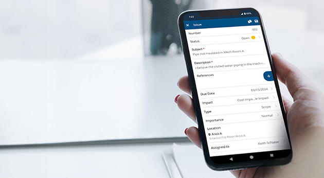 A hand holds a smartphone displaying a construction issue report on the Trimble ProjectSight mobile app.
