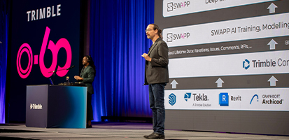 A presenter stands before a large digital screen detailing construction software workflows at the Trimble 0-60 Start-Up challenge.