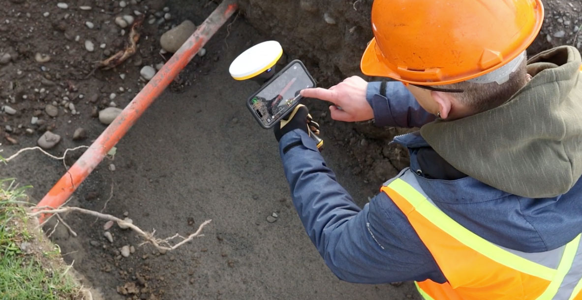 Worker on a jobsite holding a mobile phone with sitevision software attached to a trimble antenna