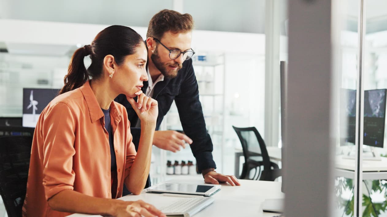 A man and woman in an office setting collaborating while looking at a computer screen together.