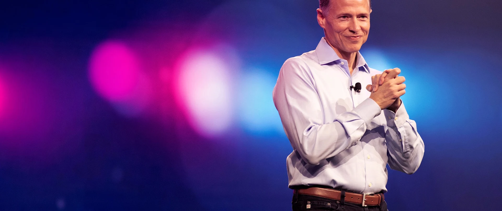 Rob Painter, Trimble President and CEO, smiling on stage during a presentation with pink and blue bokeh lights in the background.