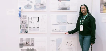 A previous winner of the SketchUp Ascent Challenge proudly stands in front of her creation, displayed via printouts hung up on a wall. 