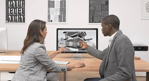 A man and a woman collaborate on an architectural 3D model using Trimble SketchUp software on a desktop monitor in a modern office.