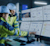 Two engineers in safety gear analyze data on multiple monitors displaying charts and graphs, reflecting a high-tech, focused work environment.