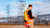 A worker in an orange vest with a Trimble geospatial device looks at a tablet near power lines.
