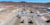 Aerial view of an outdoor construction expo in a desert, featuring heavy machinery like bulldozers, excavators, white tents, and event attendees.
