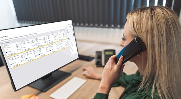 A woman on a phone call views drawing sets in Trimble ProjectSight construction management software on her computer screen.