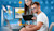 A man and a woman in an office setting are looking at a laptop and two computer monitors displaying 3D models with a blue and yellow digital overlay.