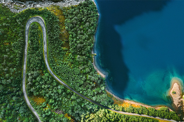 Aerial view of winding road in forest next to sea