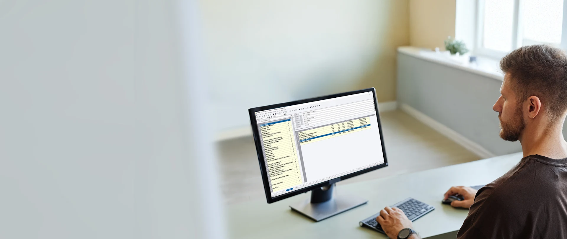 A person with short blond hair and a beard sits at a desk, looking at a computer screen displaying Accubid Classic.